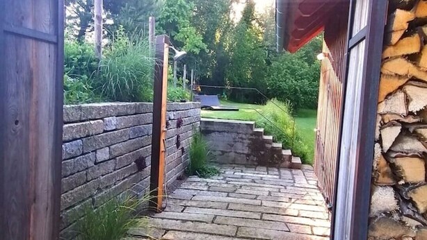 Una escalera de piedra que conduce a una puerta de madera, rodeada de un muro de piedra y vegetación.