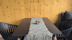 A dining table with a woven table runner, two black chairs, and a wooden wall in the background. - Tiny House Nr.1 - Wird Noch Bearbeitet - Provisorisch Erstellt (Bad Wurzach)