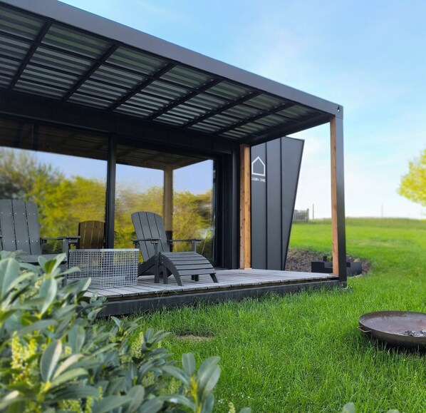 A modern outdoor seating area with a covered patio, a metal grill, and a sign indicating a cabin.