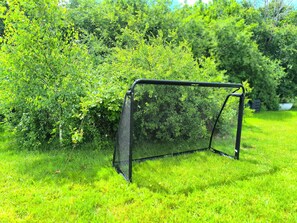 Um gol de futebol em uma área gramada, com vegetação verde densa ao fundo.