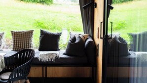 A cozy seating area with a bench, pillows, and a chair, overlooking a grassy landscape through large windows. - Tiny House Nr.1 - Wird Noch Bearbeitet - Provisorisch Erstellt (Bad Wurzach)