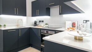 A modern kitchen with dark cabinetry, gold handles, a stainless steel sink, and a white countertop.