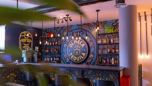 A bar area with a central circular sign reading "OLMECA TEQUILA," surrounded by shelves of bottles and a patterned wall. - Boho Boutique Hotel (Amman)