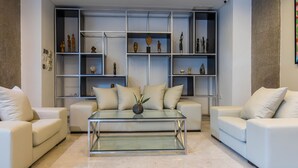 A modern living room with a glass coffee table, white sofas, and a built-in shelving unit with decorative items. - Boho Boutique Hotel (Amman)