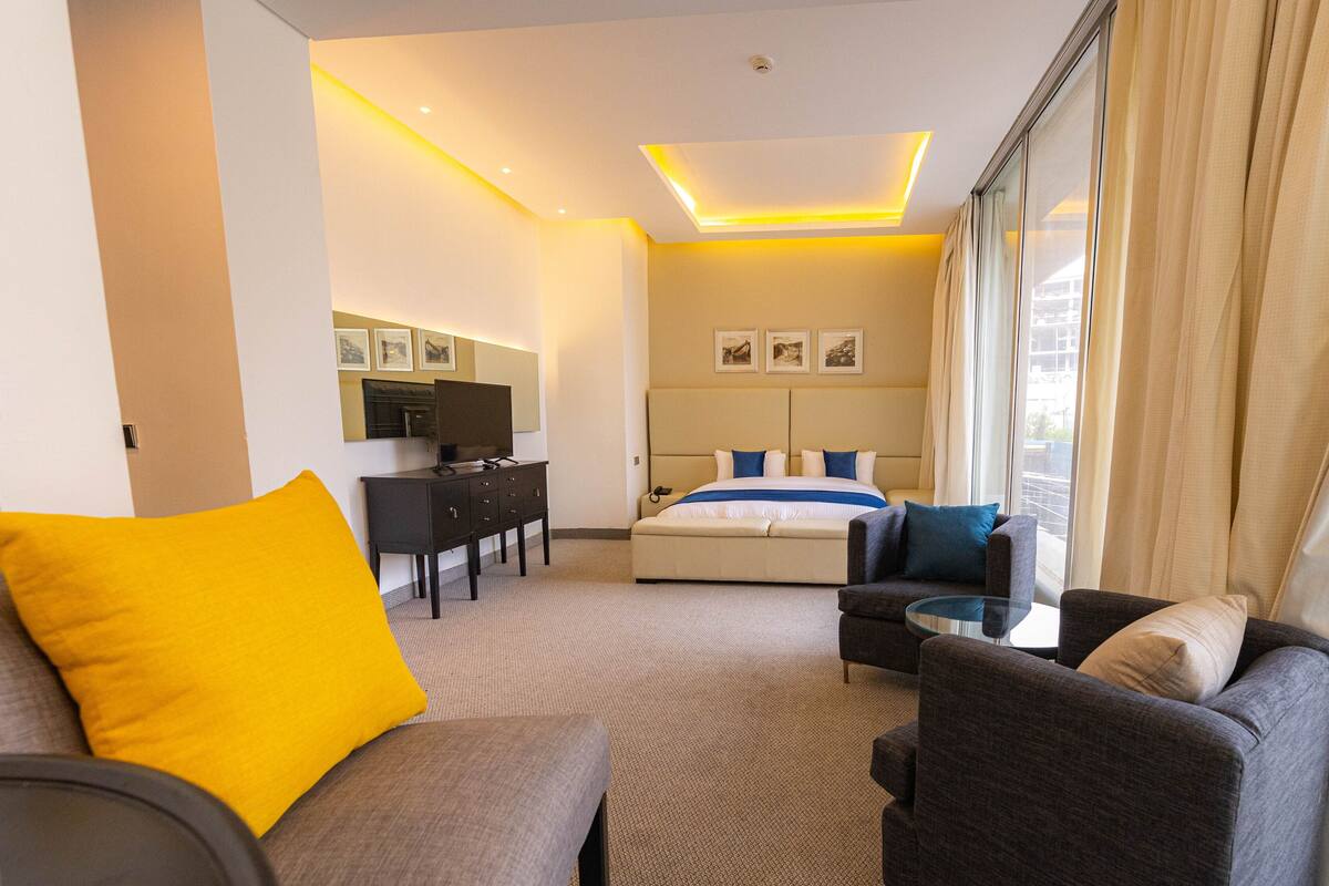 A hotel room with a bed, a desk, a TV, a sofa, and a window with curtains.