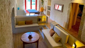 A cozy, semi-open living space with a stone wall, a sofa set, a small table, and a window with red shutters. - Torre Bertrana by Duquessa Hotel Collection (Pals)