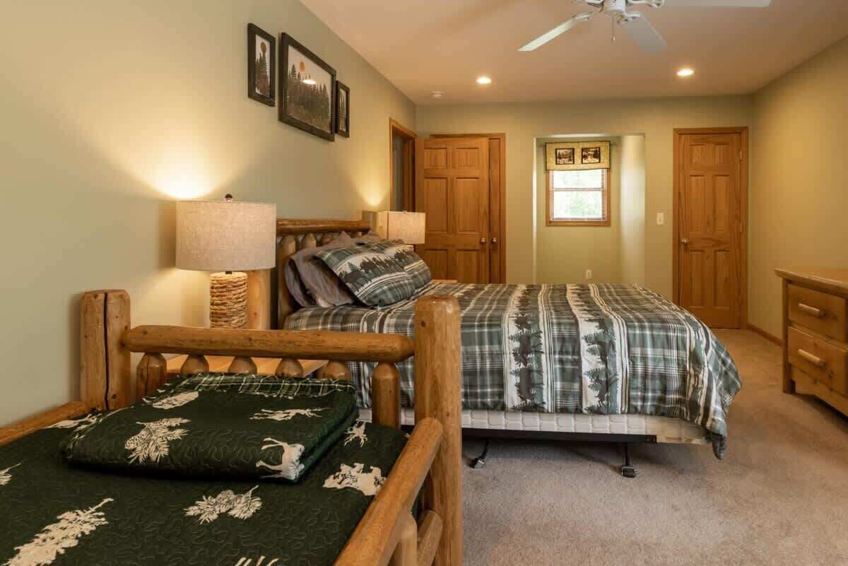 A bedroom with two beds, wooden headboards, a ceiling fan, and a window with a view.