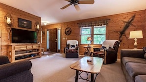 Een gezellig interieur van een chalet met een televisie, een houten entertainmentkast, een bijzettafeltje en comfortabele zithoek.