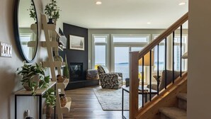 Amplia zona de estar con chimenea, un espejo grande y vista al mar a través de ventanas amplias.