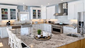 Una cocina moderna con armarios blancos, encimeras de granito, electrodomésticos de acero inoxidable y una isla central con asientos.