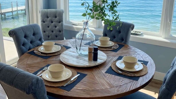 Un comedor con una mesa redonda, seis sillas y vista al agua.