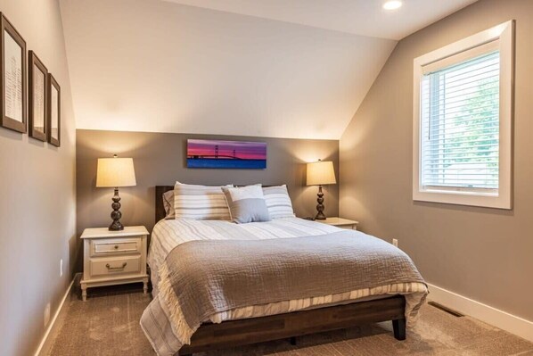 A bedroom with a bed, nightstands, a painting, and a window.