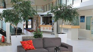 A modern lobby with a grey sofa, a wooden coffee table, and two large potted plants. - Kvarntorgets Vandrarhem (Uppsala)