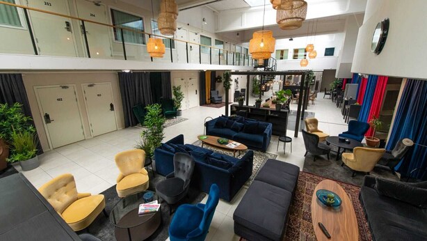 A spacious lobby with multiple seating areas, including sofas and armchairs, and a high ceiling with hanging lights. - Kvarntorgets Vandrarhem (Uppsala)