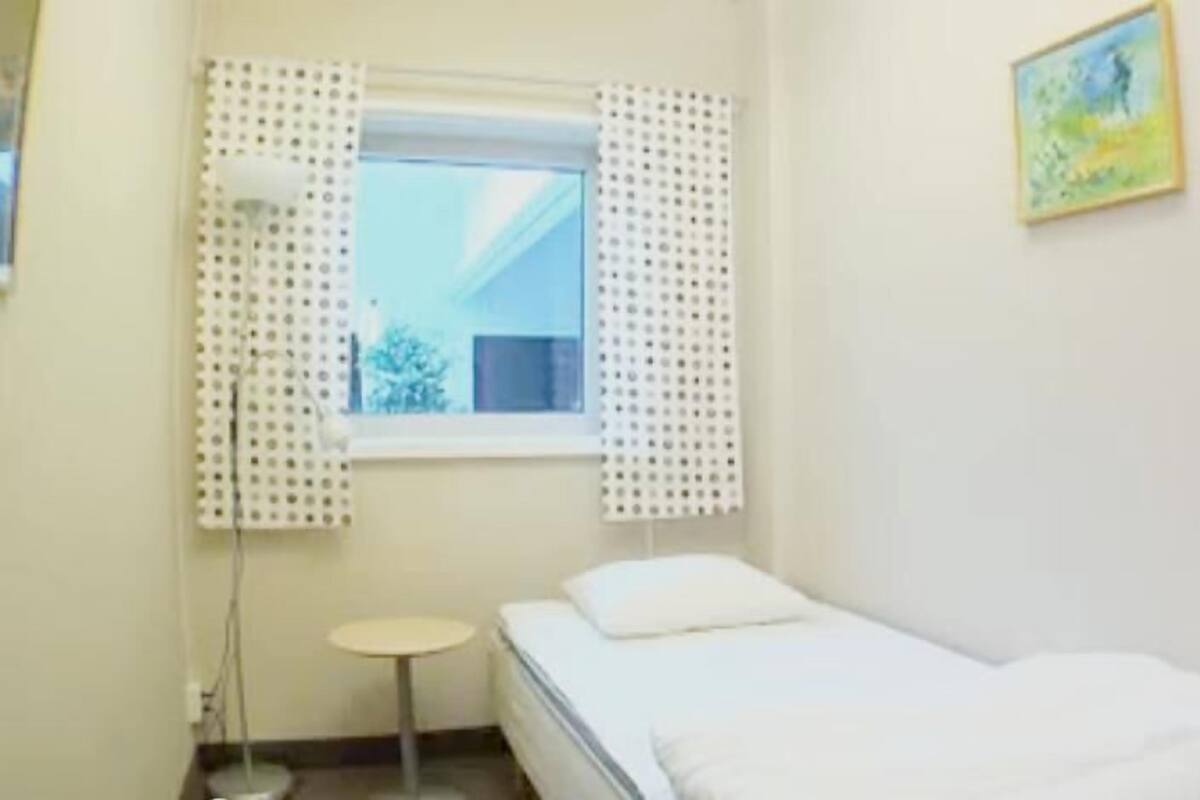 Ein kleines, sauberes Zimmer mit einem Einzelbett, einem kleinen Tisch und einem Fenster mit Vorhängen.