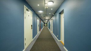 A long, narrow hotel corridor with blue walls, carpeted floors, and doors numbered 12. - Kvarntorgets Vandrarhem (Uppsala)