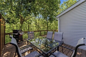 An outdoor deck with a glass-top table, chairs, and a grill.