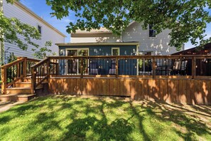A wooden deck with a staircase leading to a covered area, surrounded by a lawn and trees.