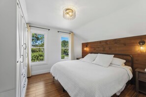 A bedroom with a wooden headboard, a white bedspread, and a window with a view of greenery.