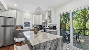A modern kitchen with a marble island, stainless steel appliances, and a large sliding glass door to a deck. - Château Ravine, backing onto a beautiful tree-filled ravine  (Niagara-on-the-Lake)