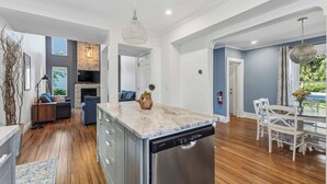 A modern kitchen with a dishwasher, a dining area with a table and chairs, and a living room with a sofa and fireplace. - Château Ravine, backing onto a beautiful tree-filled ravine  (Niagara-on-the-Lake)