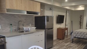 A modern kitchen with a stainless steel refrigerator, a sink, and wooden cabinets. There is a dining area with a white table and chairs. - Cozy and modern bachelor suite with kitchenette and bath  (Guelph)