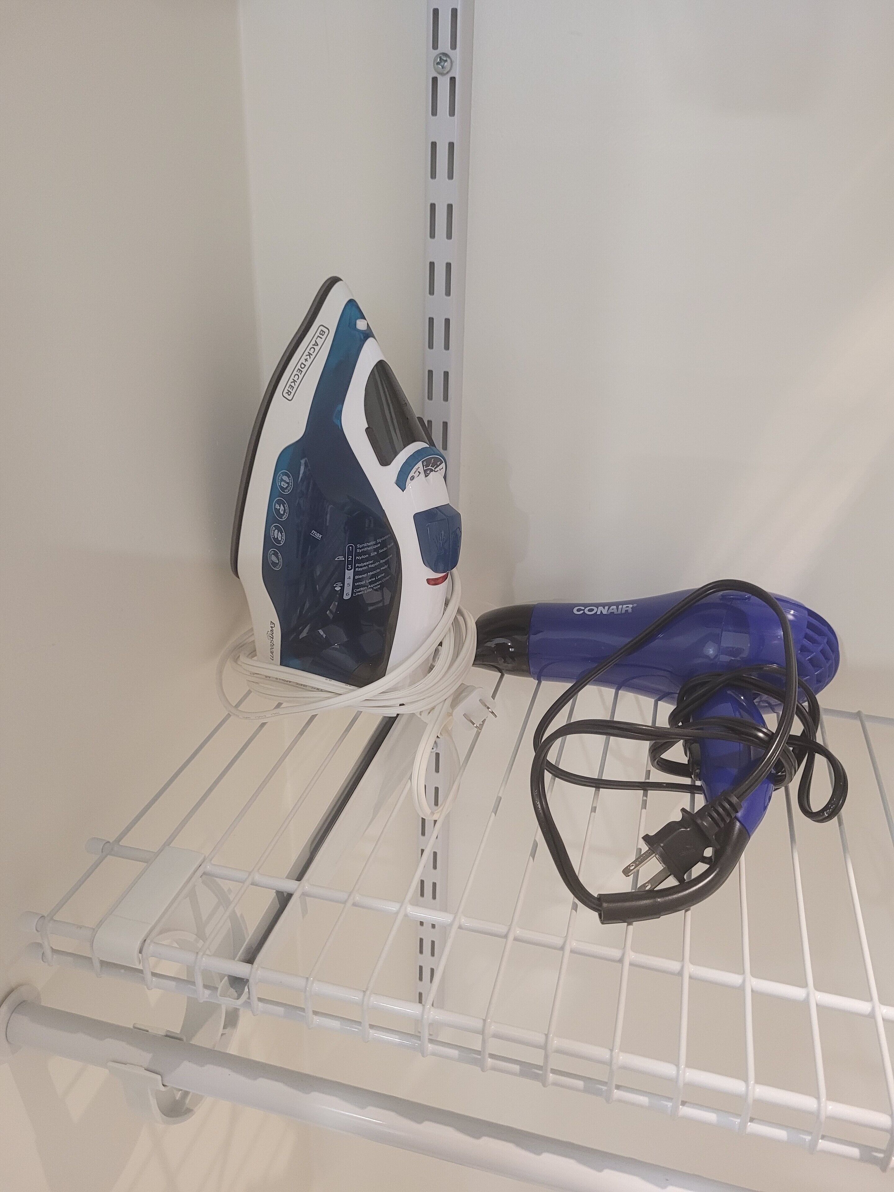 A white metal shelf with a blue iron and a blue hairdryer on it.