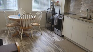 A modern kitchen with white cabinets, a built-in oven, and a coffee maker. There is a dining area with a table and chairs. - Cozy and modern bachelor suite with kitchenette and bath  (Guelph)