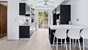 A modern kitchen with a central island, white bar stools, and a view of the outdoors. - Gav5: New Modern Condo Walking Distance to Beach (Tamarindo)