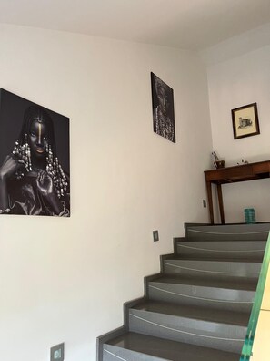 A staircase with a handrail, a wall-mounted picture frame, and a small table with a bottle and glasses.