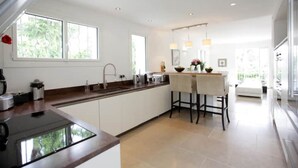 Una cucina moderna con isola centrale, zona pranzo con sgabelli da bar e ampie finestre che lasciano entrare luce naturale.