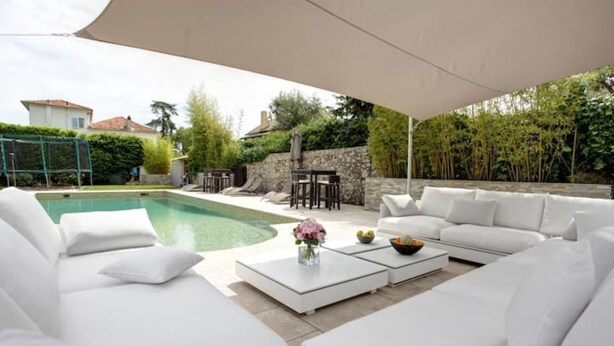 Area piscina con divano bianco, tavolino con un vaso di fiori e vista sulla piscina.