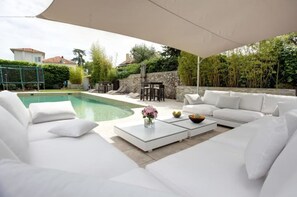 A poolside area with a white sofa set, a table with a vase of flowers, and a view of a swimming pool. - Charming villa close to Beach and old Antibes. (Antibes)