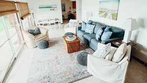 Un salón espacioso con un ventanal grande, un sofá azul, un sillón blanco y una mesa de centro.