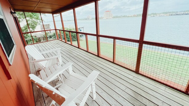 Un espacio al aire libre cubierto con vista a un cuerpo de agua, que cuenta con una terraza de madera y sillas blancas.