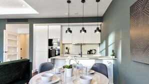 A modern kitchen with white cabinets, a dining table set with bowls and glasses, and pendant lights. - Portobello Rd - North Ken by Viridian Apartments (London)