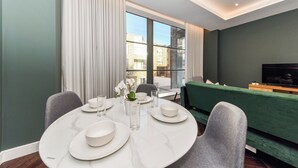 A modern dining area with a round table set for four, a green sofa, and a television in the background. - Portobello Rd - North Ken by Viridian Apartments (London)