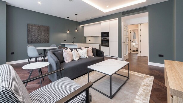A modern living room with a sofa, coffee table, and chairs. There is a kitchen area with cabinets and appliances. - Portobello Rd - North Ken by Viridian Apartments (London)