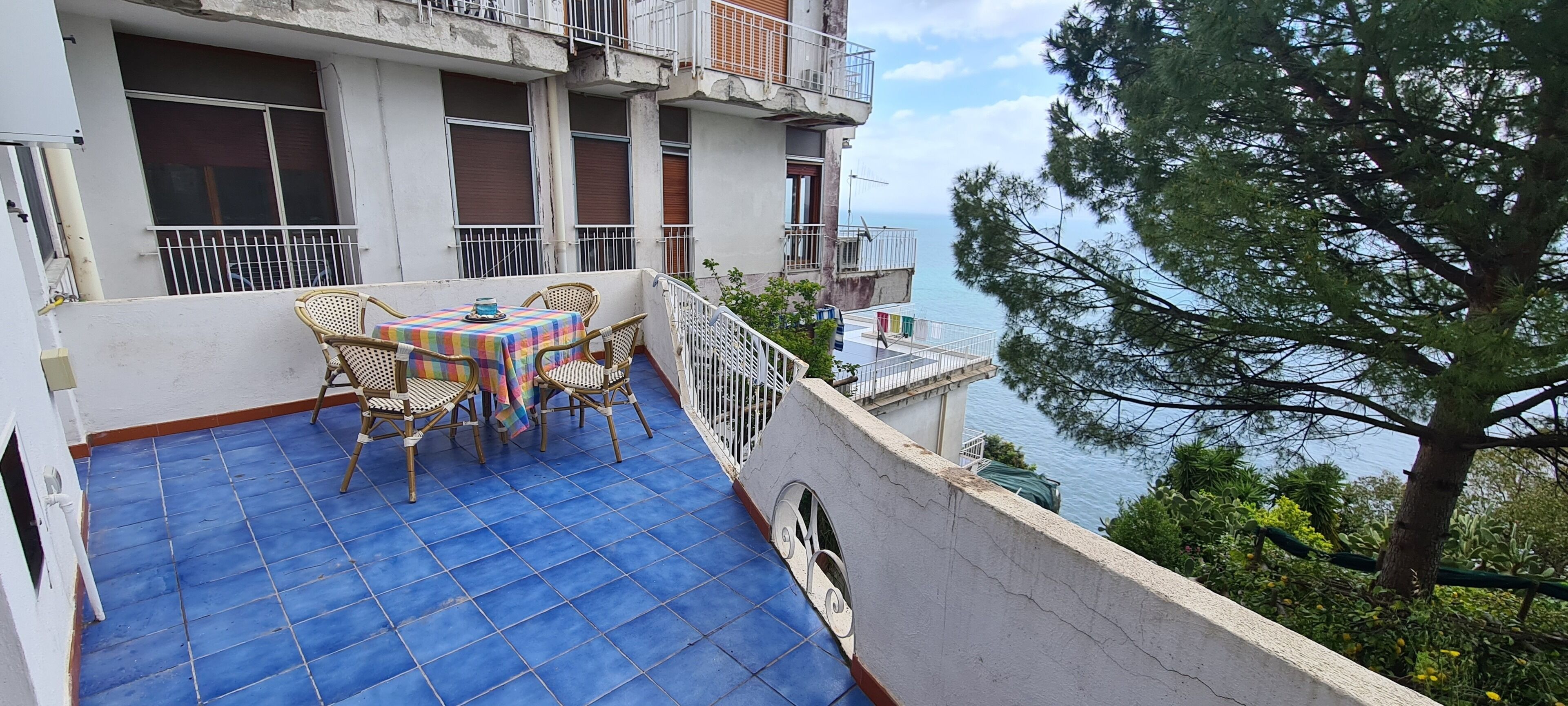 A balcony with a blue tiled floor, wicker furniture, and a table with a colorful tablecloth.
