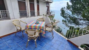 Ein Balkon mit Tisch und Stühlen, der auf ein Gewässer und viel Grün blickt.