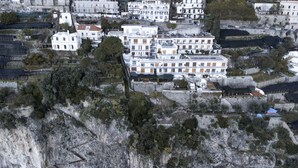 Eine Küstenstadt mit weißen Häusern, einige davon mit Balkonen, und einer felsigen Klippe im Vordergrund.