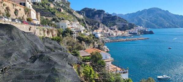 A coastal town with buildings on a hillside overlooking a clear blue sea, a marina, and rocky cliffs.