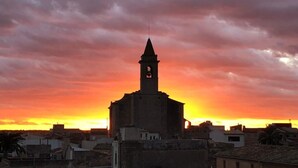 Un edificio con una torre destacada y un reloj, silueteado contra un cielo al atardecer.