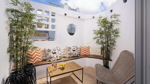 A cozy outdoor seating area with a wooden bench, a wicker chair, and a table with a fruit bowl and glasses. - Art Oasis 2-3BR Home in Historic Quarter by Portimao Pier (Portimão)