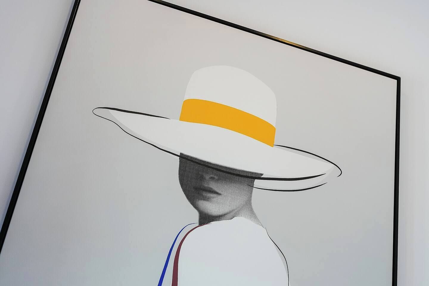 A framed artwork of a hat with a yellow band.
