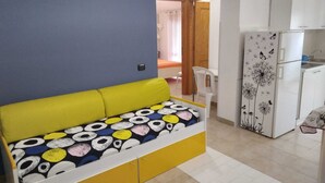 Ein kompakter Wohnbereich mit Schlafsofa, Kühlschrank und Essplatz.