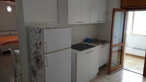 Eine kleine Küche mit weißen Schränken, einem Kühlschrank, einem Spülbecken und einer Glastür zum Balkon.