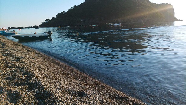 Ein Kiesstrand mit Booten und einer felsigen Insel im Hintergrund.