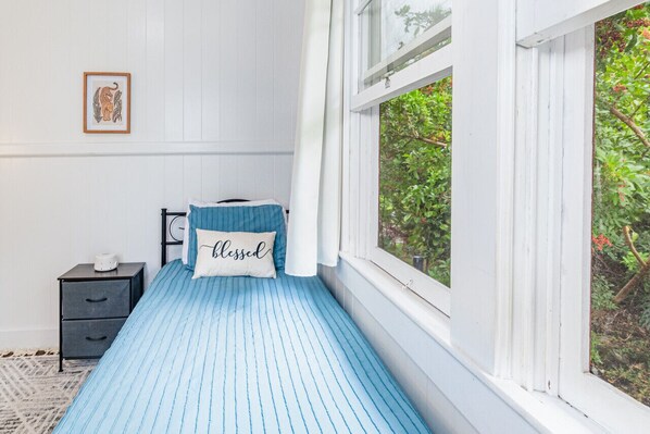 Un dormitorio pequeño y ordenado con una cama individual, una mesita de noche y una ventana con vistas a la vegetación.