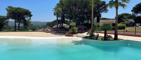 Una piscina azul cristalina rodeada de palmeras y vistas a un paisaje montañoso.